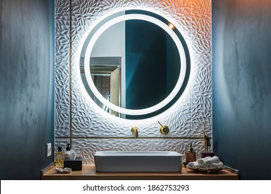 Modern bathroom interior with white wash basin, golden faucet and round illuminated mirror. - Shutterstock ID 1862753293