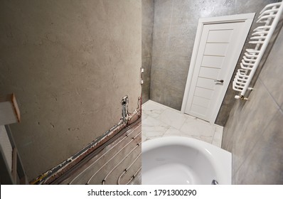 Modern Bathroom With Marble Floor And White Door Before And After Refurbishment. Comparison Of Old Restroom With Underfloor Heating Pipes And New Bathroom With Heated Towel Rail And While Bathtub.