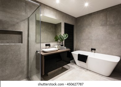 Modern bathroom with a shower area and bath tub including a wall mirror beside a fancy plant near a tap and sink over the wooden counter and dark cupboard