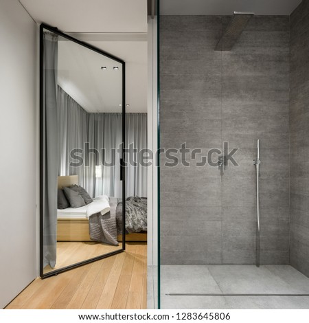 Modern bathroom with spacious walk in shower next to elegant bedroom with glass door