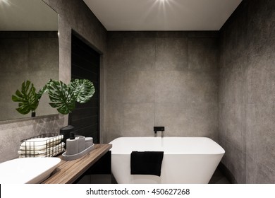 Modern Bathroom Wall Made In Dark Color Tiles Which Covered The Bathtub And Towels Near The Fancy Plant