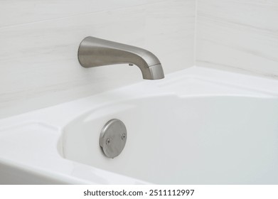 A modern bathtub with a sleek faucet and drain, set against a light-colored wall. - Powered by Shutterstock