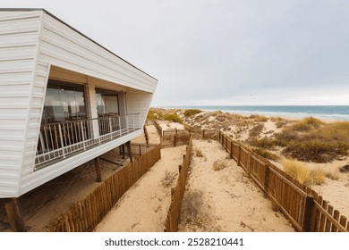 Modern beachfront restaurant on stilts overlooks sandy dunes and the ocean. - Powered by Shutterstock