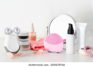 Modern Beauty Routine With Gadgets. Cleanser And Microcurrent Devices, Gua Sha Roller, Professional Cleansing Cloths , Natural Oil And Serum, Cream And Masks On White Table With Mirror.