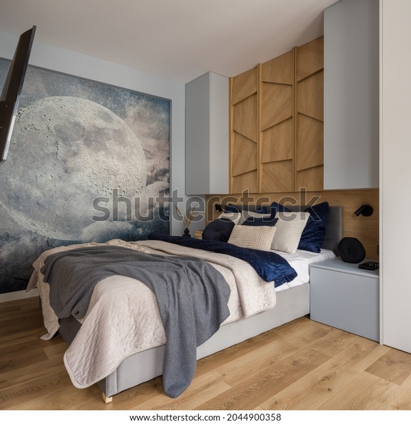 Modern bedroom with comfortable bed, wood décor and stylish moon wallpaper mural.