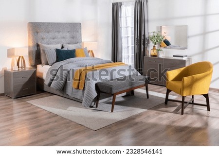 A modern bedroom featuring a large bed, a yellow chair, a dresser, and a wooden bench, a cozy interior space