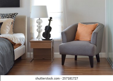 modern bedroom interior with orange pillow on grey chair and bedside table lamp at home