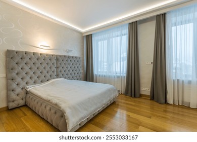 Modern bedroom with light walls, parquet floor. A wide bed with a gray padded headboard. - Powered by Shutterstock