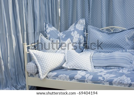 Modern bedroom with lightblue curtains and textured cushions.
