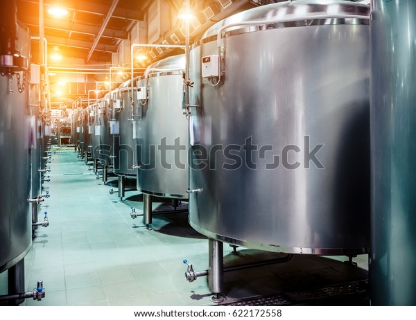Modern Beer Factory. Rows\
of steel tanks for beer fermentation and maturation. Spot light\
effect