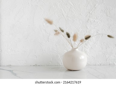 Modern Beige Ceramic Vase With Dry Fluffy Flowers On Marble Table Near A White Textured Wall. Copy Space.Minimal Scandinavian Interior. Neutral Trendy Colors Interior Decoration .