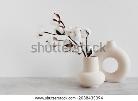 Modern beige ceramic vases with dry  cotton branches on gray table near a white wall. Copy space.Minimal Scandinavian interior. Neutral trendy colors interior decoration .