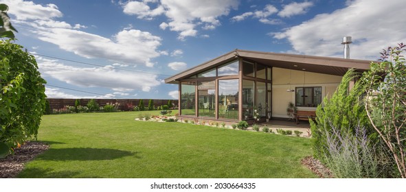 Modern beige country house with panoramic windows and green lawn in beautiful garden.
