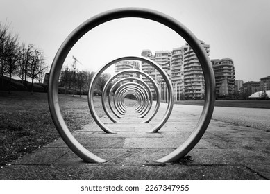 Modern bicycle parking area in an urban park in Milan, Italy. The structure is made of several concentric circles in metal, with vanishing point. Monochromatic.