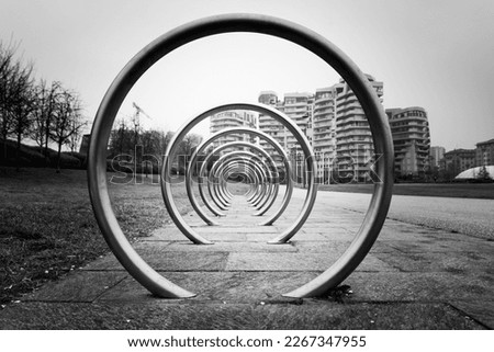 Modern bicycle parking area in an urban park in Milan, Italy. The structure is made of several concentric circles in metal, with vanishing point. Monochromatic.