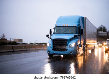 Modern Big Rig Blue Semi Truck With Covered Semi Trailer Driving On Twilight Rainy Wet Highway With Headlight Traffic Reflection Of The Rain Drops