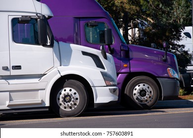 Modern Big Rigs Semi Trucks Stand In A Row In The Truck Stop Parking Lot Waiting For The End Of The Rest Time And Continuing The Way In The Specified Direction For The Delivery Of Commercial Goods