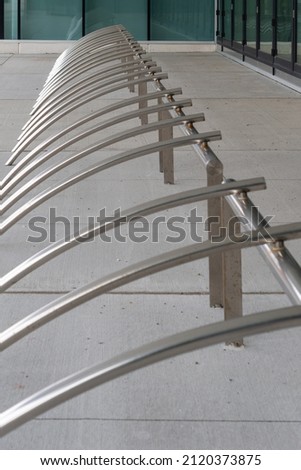 A modern bike rack made of galvanized steel. The street parking bicycle rack is empty and has a pattern of curved half circle shapes on a campus parking lot. The gray holder is near a glass building.