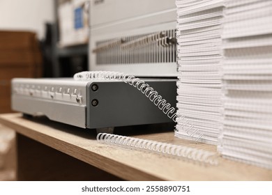 Modern binding machine, stacks of notebooks and double loop wire binding spines on wooden table indoors, closeup - Powered by Shutterstock