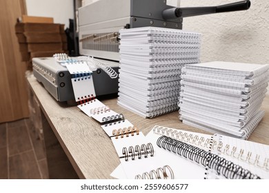 Modern binding machine, stacks of notebooks and double loop wire binding spines on wooden table indoors, closeup - Powered by Shutterstock