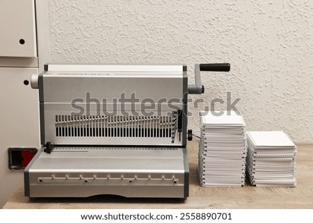 Modern binding machine and stacks of notebooks on wooden table indoors