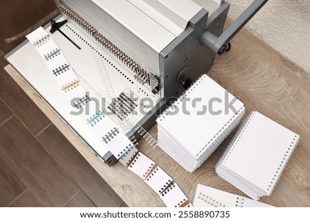 Modern binding machine, stacks of notebooks and double loop wire binding spines on wooden table indoors, above view