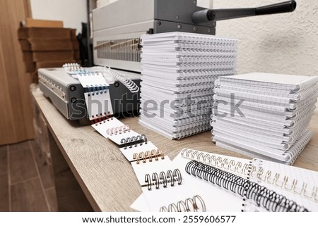 Modern binding machine, stacks of notebooks and double loop wire binding spines on wooden table indoors, closeup