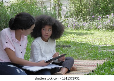 Modern Black American Mother And Daughter Family Are Relax Talking While Holding Tablet Computer To Do Homework At Backyard Garden House Background, Copy Space.