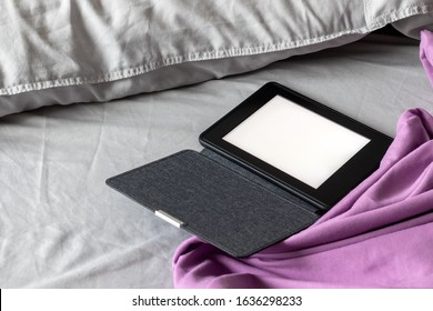 A Modern Black E-reader Electronic Book With A Blank Screen In A Denim Cover On A Gray And Purple Bed. Mockup Tablet On Microfiber Bedding