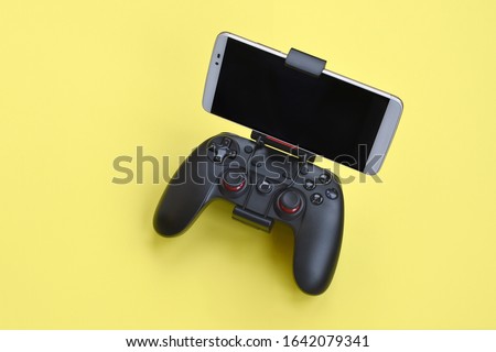 Modern black gamepad for smartphone on yellow background. Mobile video gaming device