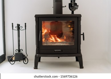Modern Black Metal Fireplace Burning Wood Stove. Firewood in Loft Contemporary House on White Wall Background. Elegant Fire Decoration for Residential Apartment. Stylish Bonfire with Copy Space