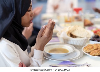 Modern Black Muslim Woman Praying Before Having Iftar Dinner Together With Multiethnic Family During A Ramadan Feast At Home