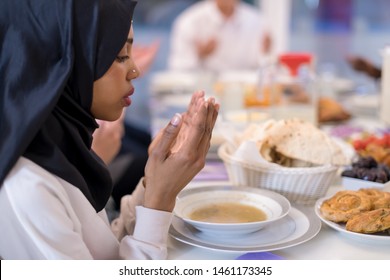 Modern Black Muslim Woman Praying Before Having Iftar Dinner Together With Multiethnic Family During A Ramadan Feast At Home
