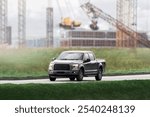 Modern black pickup truck driving on suburban road with industrial backdrop