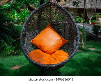 Modern Black Rattan Lounger Hanging Egg Chair With Orange Pillow In The Garden.