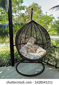 Modern Black Rattan Lounger Hanging Egg Chair With Pillow In The Garden.