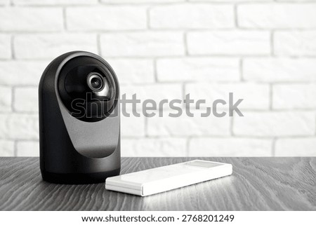 Modern black security camera and remote on a wooden table. Smart home surveillance technology