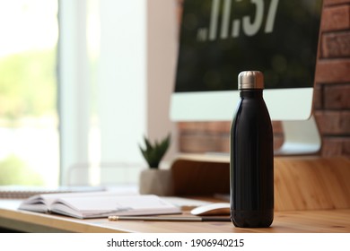Modern black thermos bottle on wooden desk at workplace. Space for text