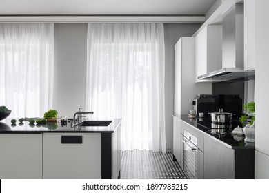 Modern black and white kitchen with big windows behind white curtains and with black and white kitchen island with sink