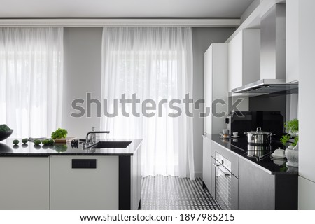 Modern black and white kitchen with big windows behind white curtains and with black and white kitchen island with sink