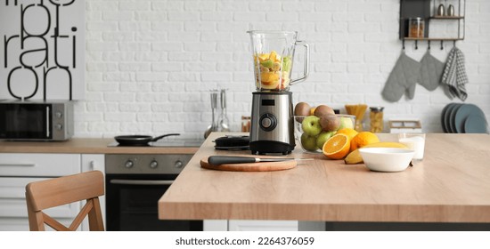 Modern blender with fresh fruits and cutting board on table in kitchen
