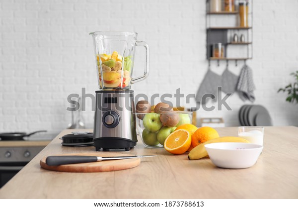 Modern blender with fresh fruits and cutting\
board on table in\
kitchen