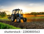 Modern blue tractor machinery plowing agricultural field meadow at farm at spring autumn during sunset.Farmer cultivating,make soil tillage before seeding plants,crops,nature countryside rural scene