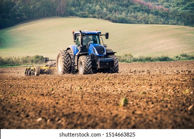 Modern blue tractor on the field during stubble-tillage cultivation after harvest with yellow equipment using GPS for precision farming in the fields of Czech Republic during sunny autumn day. 