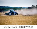 A modern blue tractor with a trailed disc harrow with a husking roller plows a field on which the spring grain crop has just been harvested. Midsummer in central Ukraine.