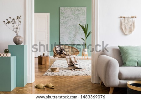Modern and bohemian composition of interior design at apartment with gray sofa, rattan armchair, wooden cubes, plaid, tropical plant, macrame and elegant accessories. Stylish home decor. Template.