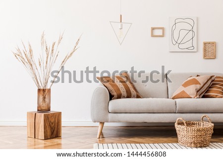 Modern boho interior of living room at cozy apartment with gray sofa, honey yellow pillows and plaid, mock up paintings, rattan basket and design personal accessories. Stylish home decor. Template.