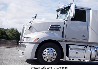 Modern Bonnet Professional Light Gray Clean Reliable New Big Rig Day Cab Semi Truck With Big Mirrors And Aluminum Steps And Fuel Tank Running On The Straight Local Road