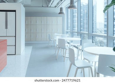 A modern break area in an office, featuring large windows that allow ample natural light to flood the space. The area is furnished with minimalist white tables and chairs. - Powered by Shutterstock