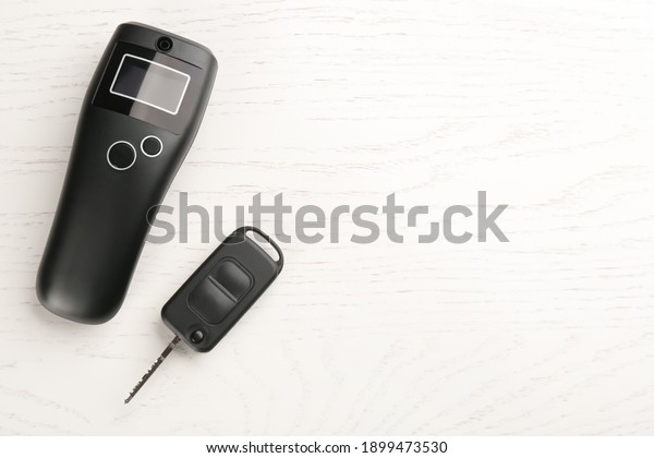 Modern breathalyzer and car key on white wooden\
table, flat lay. Space for\
text